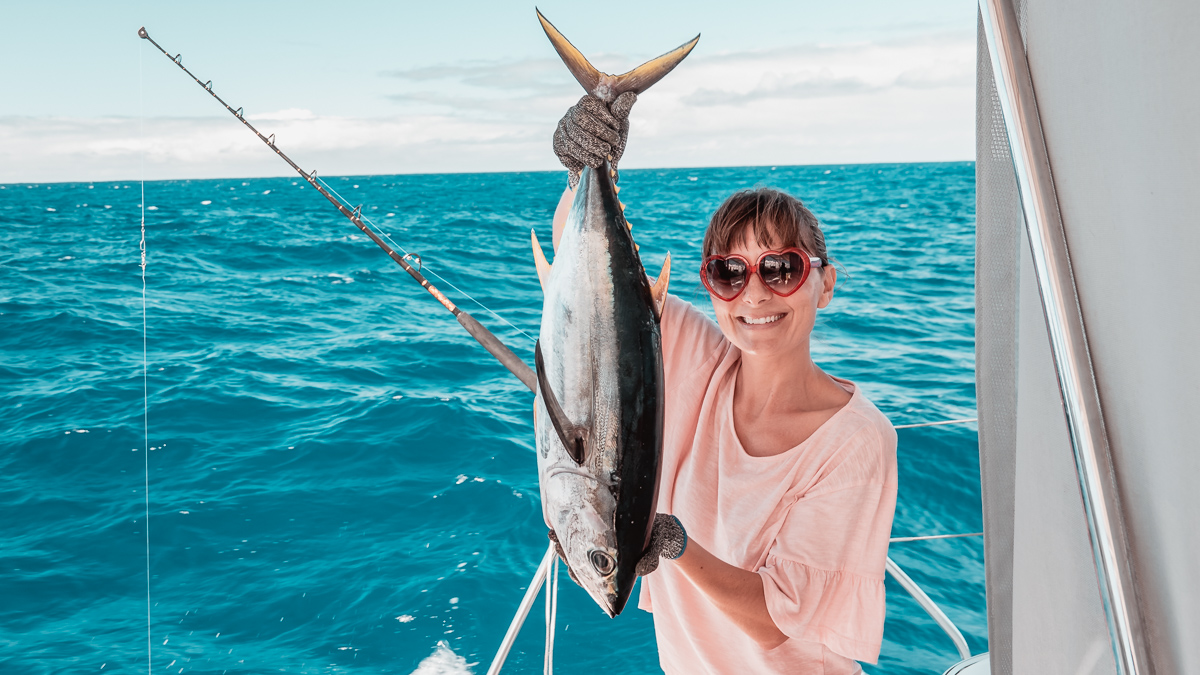 nikki wynn holding up a fresh caught tuna aboard sailing catamaran curiosity